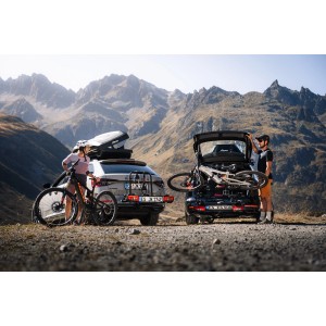Atera Strada Sport 3 Fahrradträger an zwei Autos mit Fahrrädern und Dachbox vor Berglandschaft.