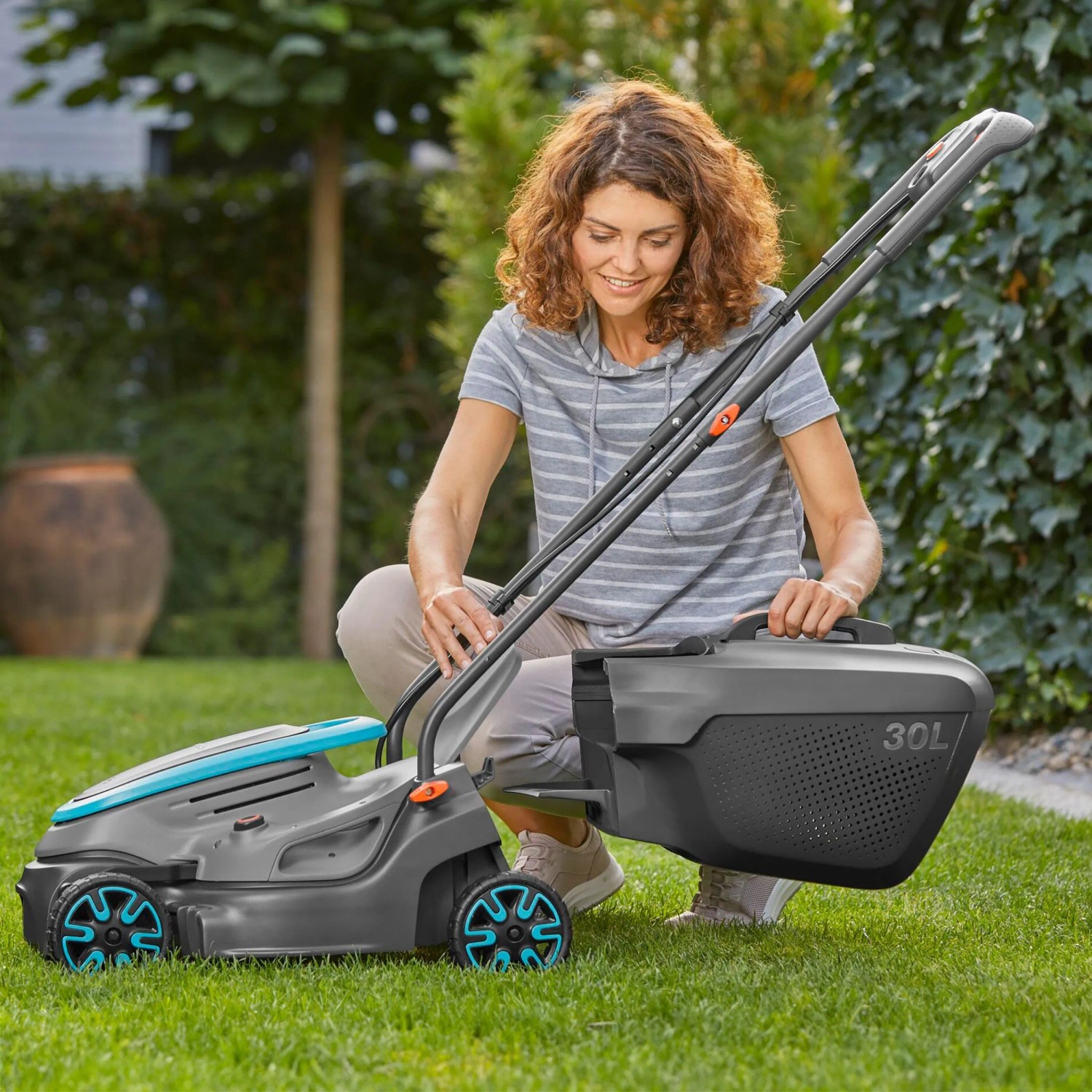 Gardena Akku-Rasenmäher PowerMax 32/18V mit Akku und Fangkorb im Garten. Frau montiert den Rasenmäher.