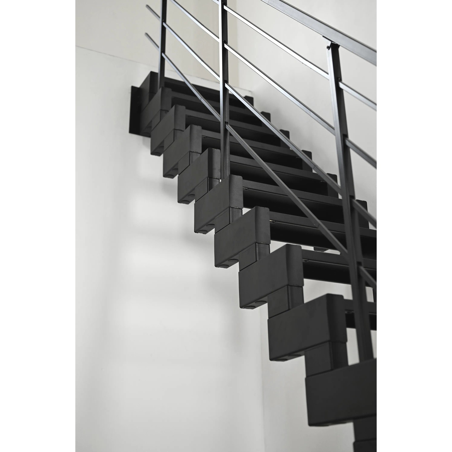 Schwarze Minka Raumspartreppe Modulario Mini Steel mit Stahlgeländer vor weißer Wand.
