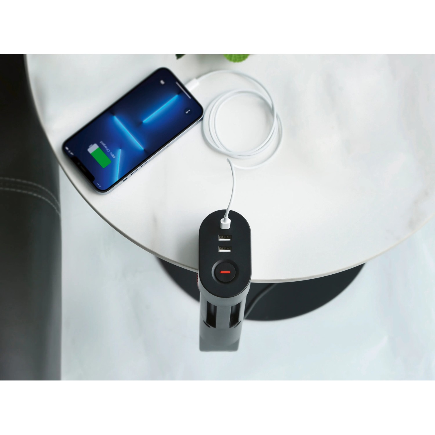 Schwarze 3-fach Steckdosenleiste mit USB-Anschlüssen und geladenem Smartphone auf einem Tisch.