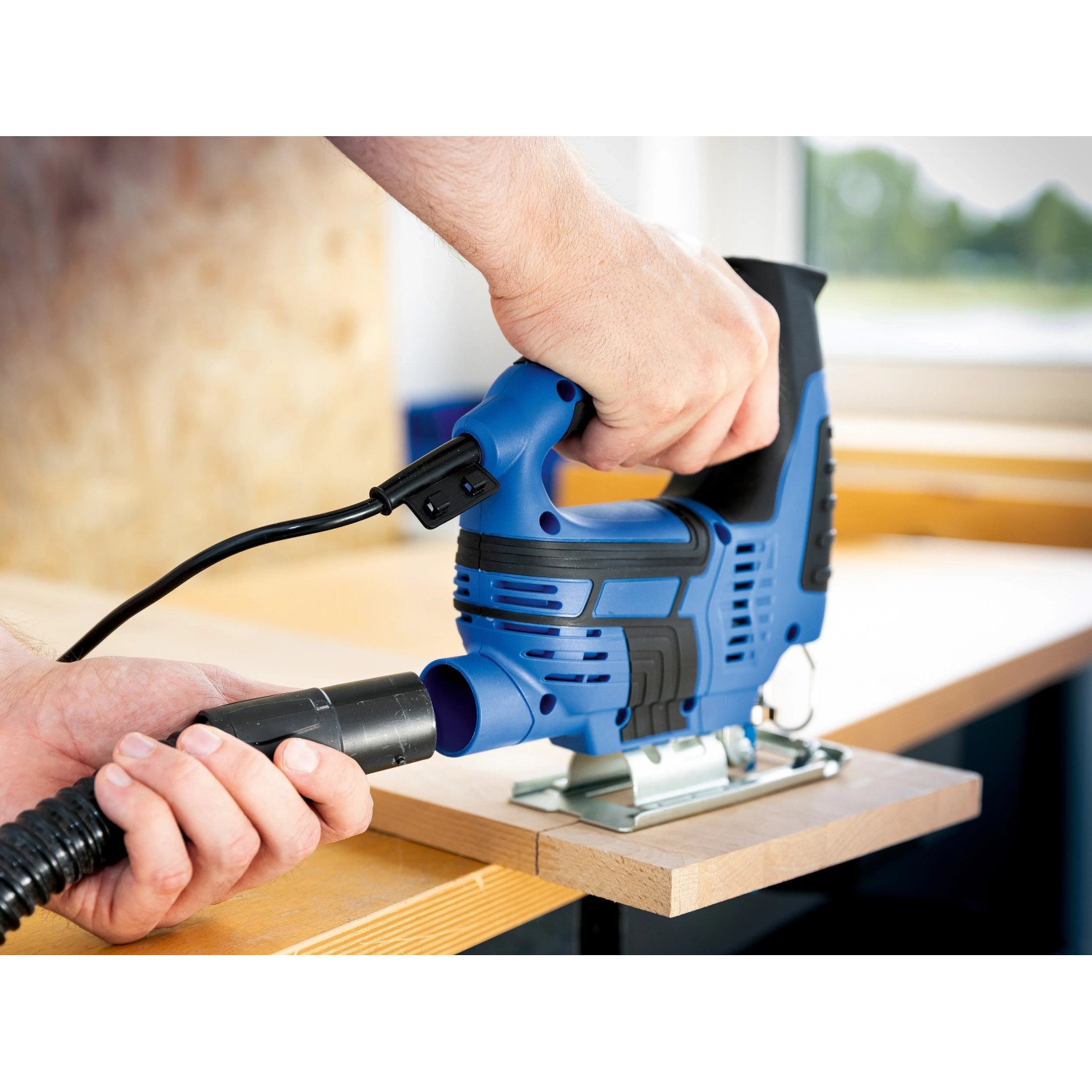 Blaue LUX Stichsäge E-STS-23 mit Staubsauger-Anschluss beim Sägen von Holz.