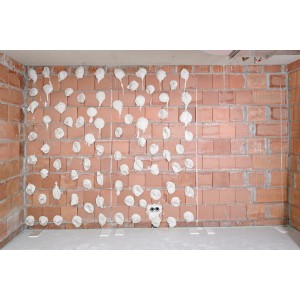 Aufgetragenes Knauf Perlfix Ansetzgips auf einer Ziegelwand, bereit für die Montage von Gipskartonplatten.