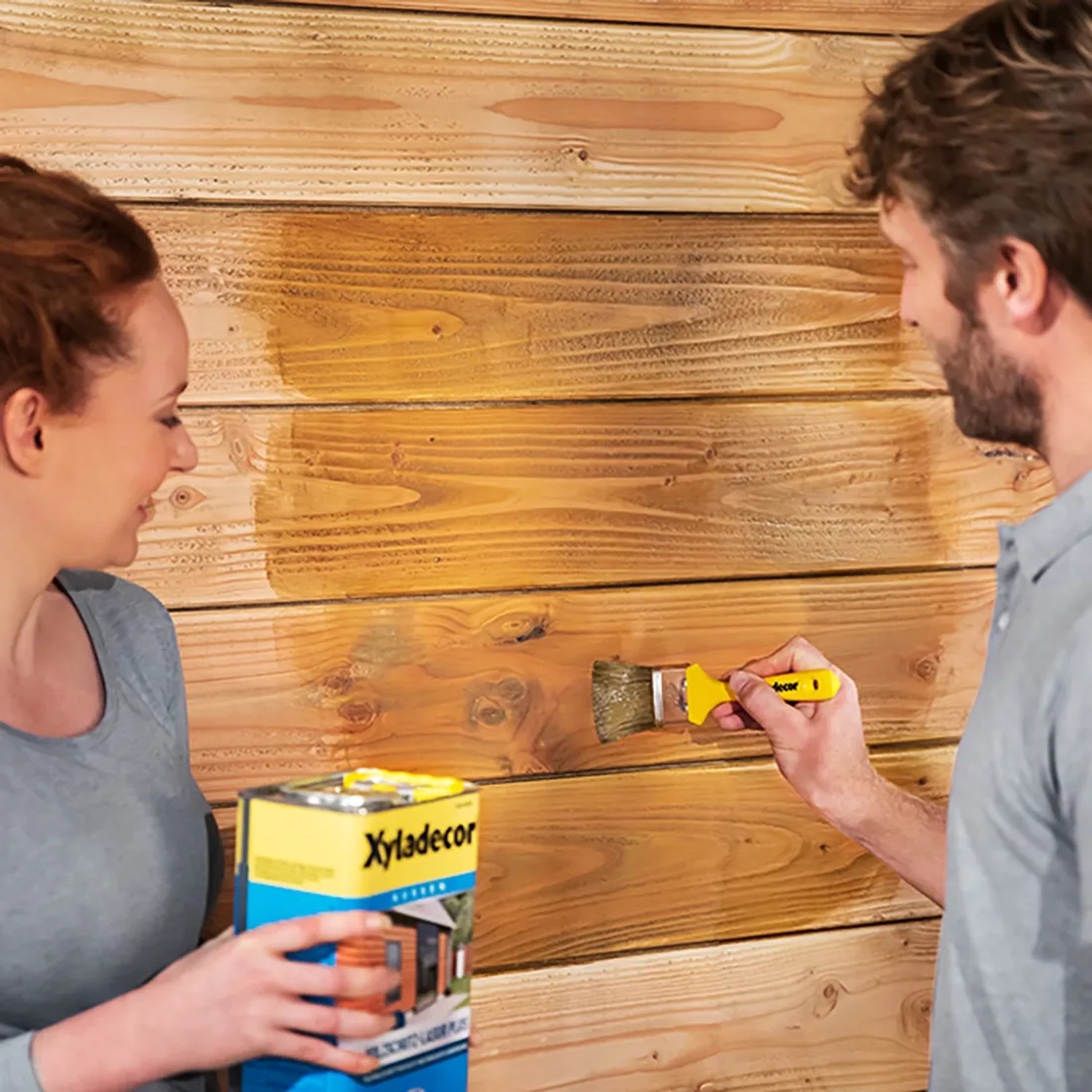 Anwender streichen Holz mit Xyladecor Holzschutz-Lasur Ebenholz. Dose der Holzlasur im Vordergrund.