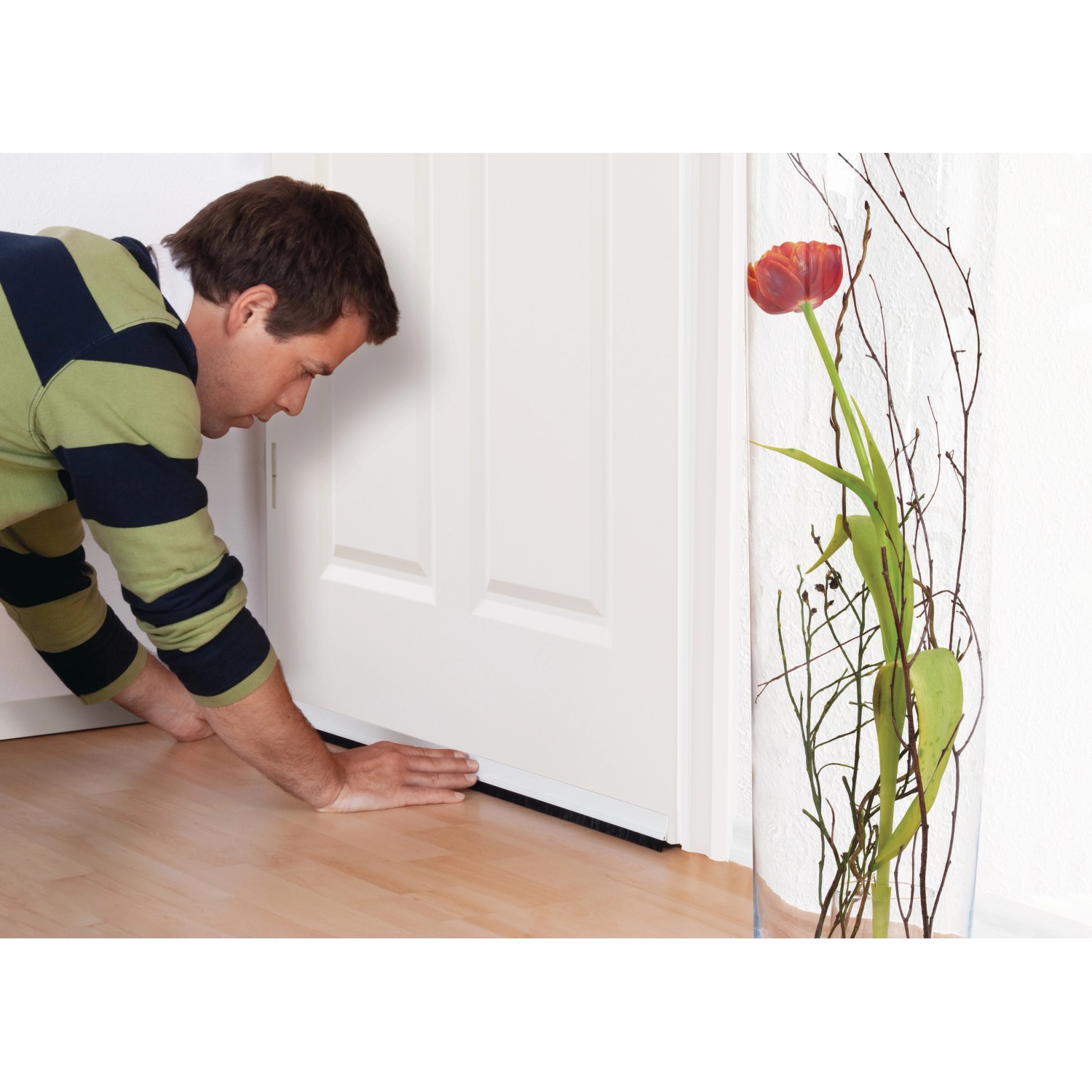 Mann montiert weiße Tesamoll Comfort Türdichtschiene an einer Tür für unebene Böden.