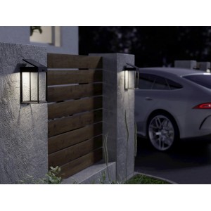 Schwarze Eglo Solar LED-Wandleuchte Suzzara mit Sensor an einer Hauswand und einem Zaun.