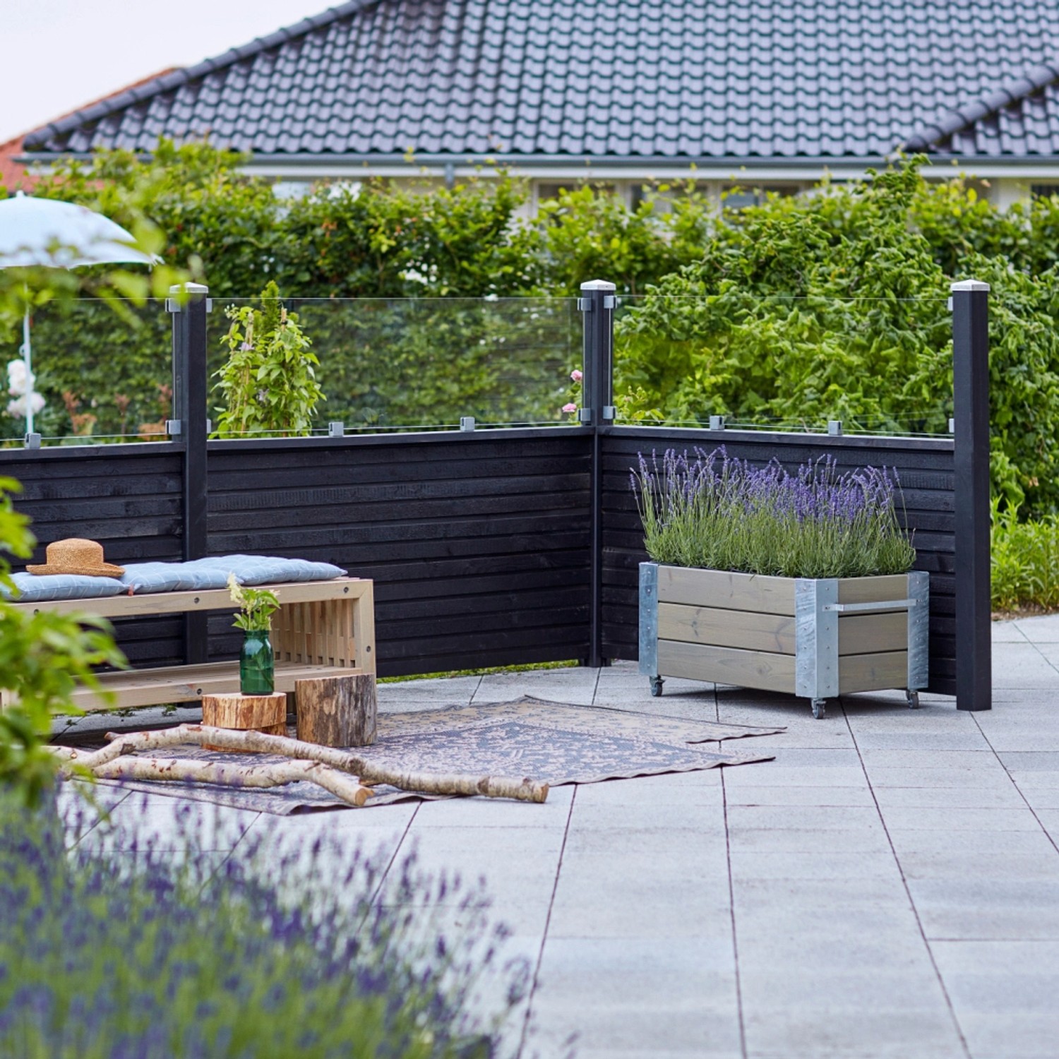 Schwarzer Sichtschutzzaun Plank aus Nadelholz mit Glaselement im Garten.