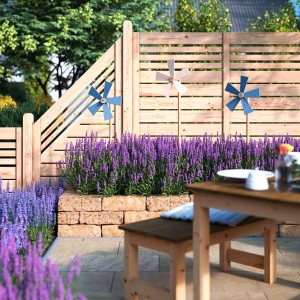 Gartenmauer aus ockerfarbenen Tuffsteinen mit Lavendel und Windrädern vor Holzzaun.