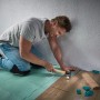 Mann verlegt Laminat mit wolfcraft Verlege-Set: Zugeisen, Schlagholz und Keile für Designboden.