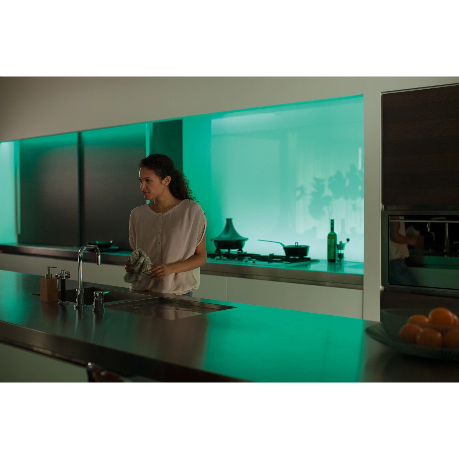 Frau in Küche mit Philips Hue Lightstrip Plus mit grüner Ambiente-Beleuchtung.