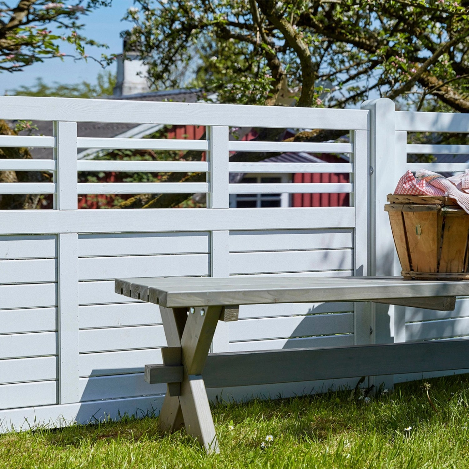 Weißer Sichtschutzzaun Decora aus Nadelholz, 180x95 cm, mit Gartenbank und Picknickkorb im Garten.