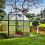 Graues Palram Canopia Gewächshaus 4,6 m² mit Fundamentrahmen im Garten.