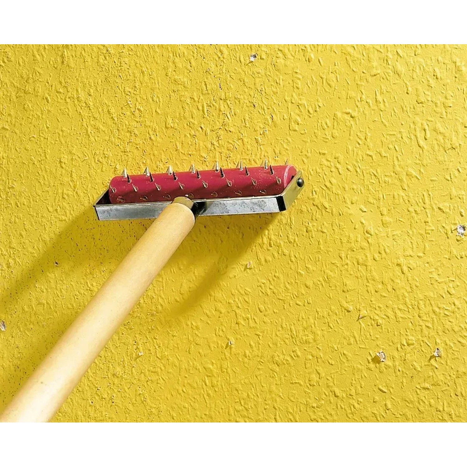 LUX Tapeten-Stachelwalze 15 cm mit Holzgriff zum Anreißen von Tapeten auf gelber Wand.