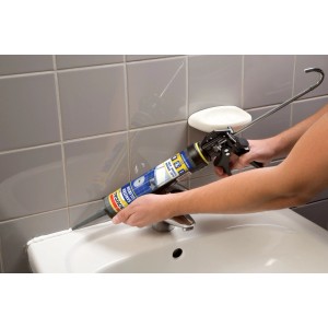 Hände dichten weißes Waschbecken mit Soudal Sanitär Silikon ab. Graue Fliesen im Bad.
