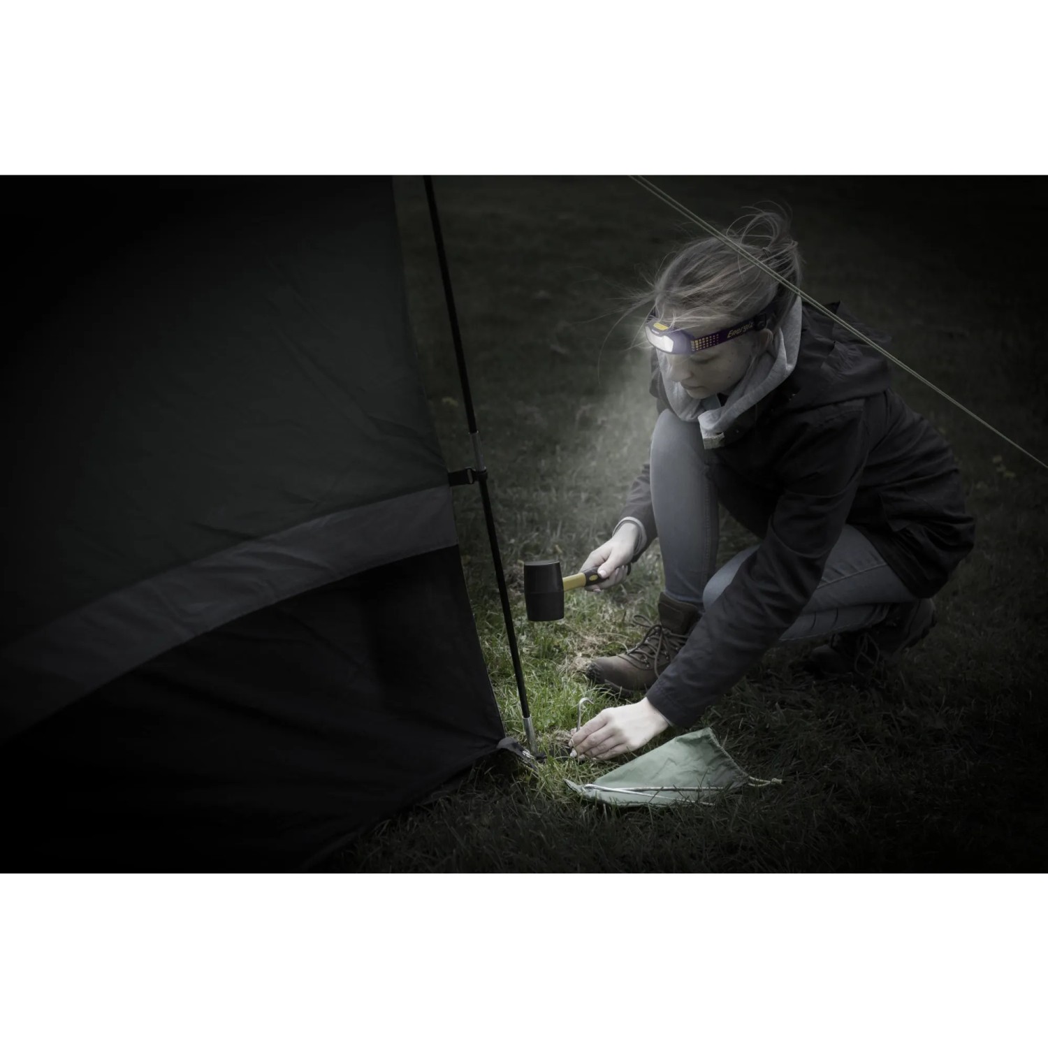 Frau beim Zeltaufbau mit Energizer Kopflampe Compact Sport Headlamp. Taschenlampe leuchtet.