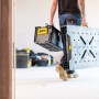 Mann trägt klappbare Stanley FatMax Werkbank (85x60cm) und Werkzeugkiste durch eine Tür.