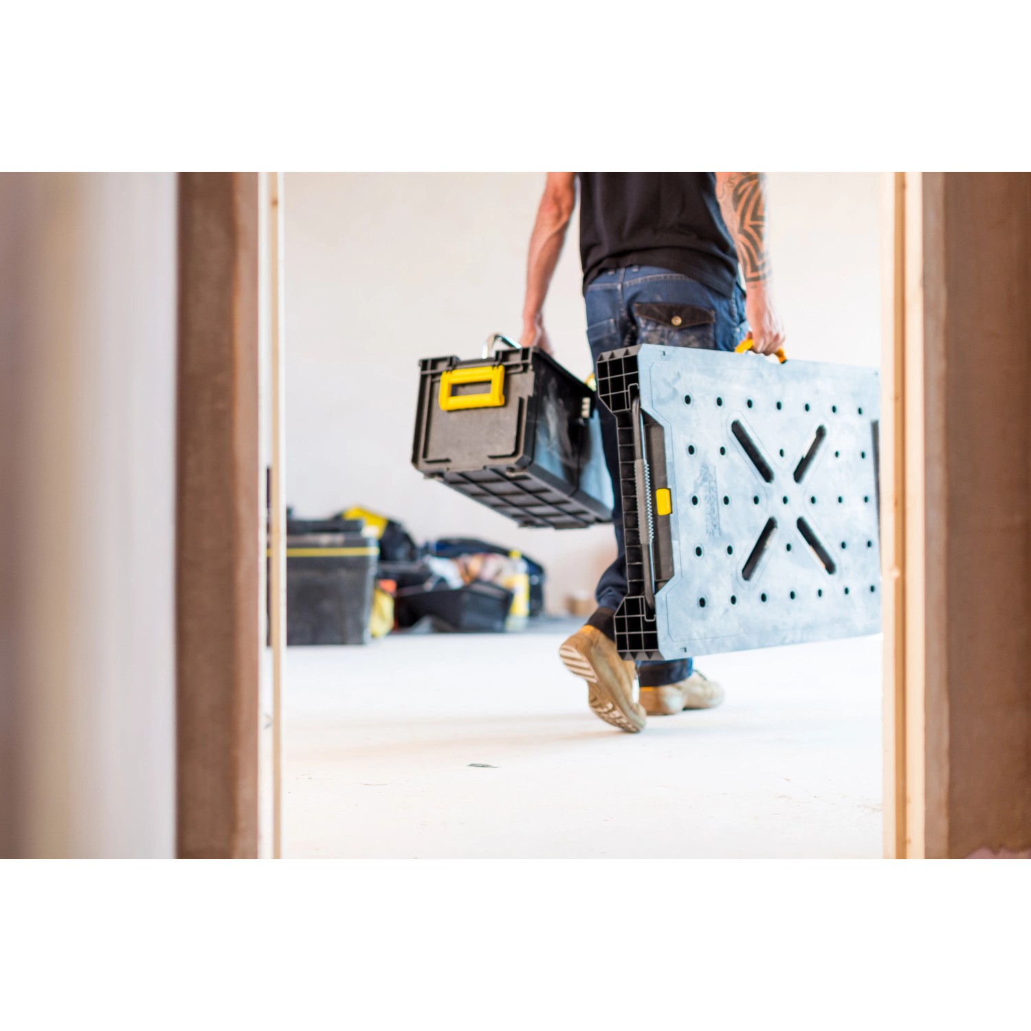 Mann trägt klappbare Stanley FatMax Werkbank (85x60cm) und Werkzeugkiste durch eine Tür.