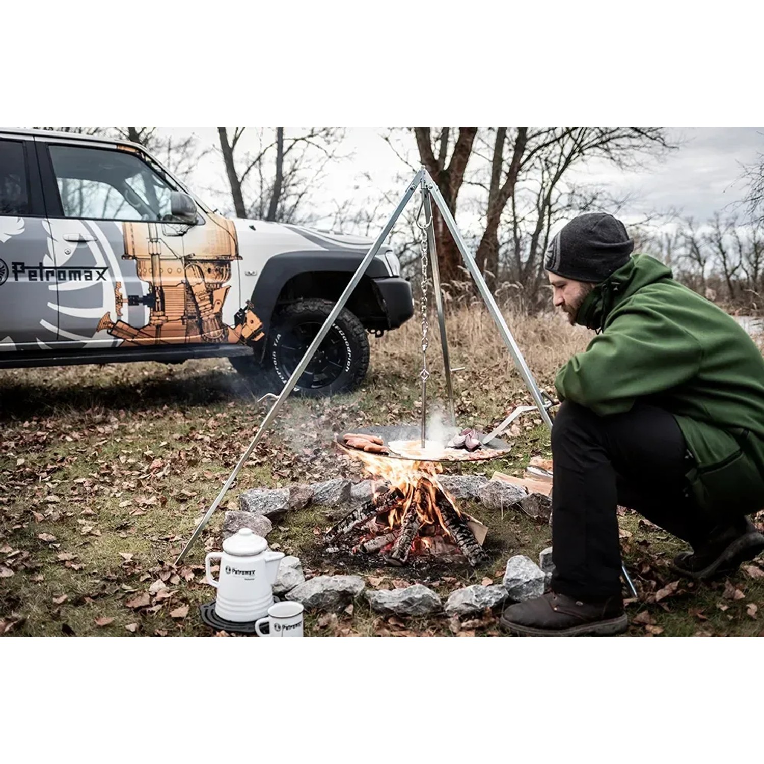 Petromax Dreibein mit Kette über Lagerfeuer beim Kochen. Grillutensil für Outdoor-Küche.