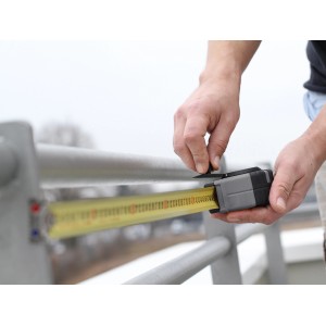 Hand misst mit LUX Taschenbandmaß Professional 10 m ein graues Geländer.