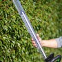 LUX Akku-Heckenschere mit Akku und Ladegerät vor grüner Hecke. Heckentrimmer mit Messerschutz.