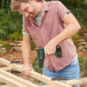 Mann bohrt mit Bosch Akku-Schlagbohrschrauber EasyImpact 18V-40 in Holz. Vielseitiger Akku-Bohrschrauber.
