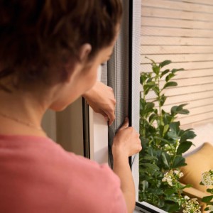 Frau befestigt anthrazitfarbenes tesa Insect Stop Fliegengitter am Fenster.