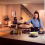 Szene mit Philips Hue White Ambiance E27 LED: Frau kocht, Paar entspannt im Wohnzimmer.