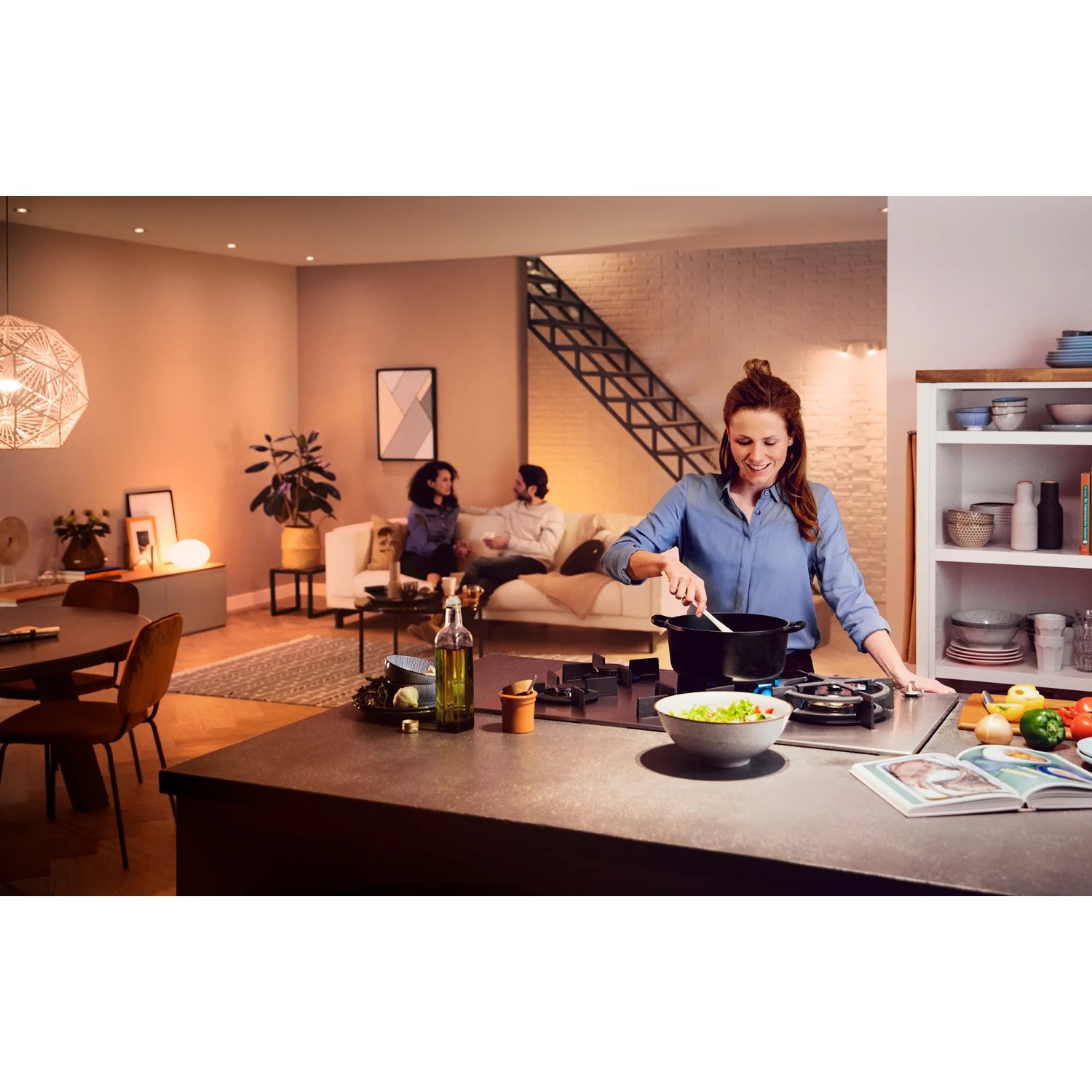 Szene mit Philips Hue White Ambiance E27 LED: Frau kocht, Paar entspannt im Wohnzimmer.