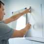 Mann befestigt Spiegel mit LUX Montageband an Wand. Doppelseitiges Klebeband für sicheren Halt.