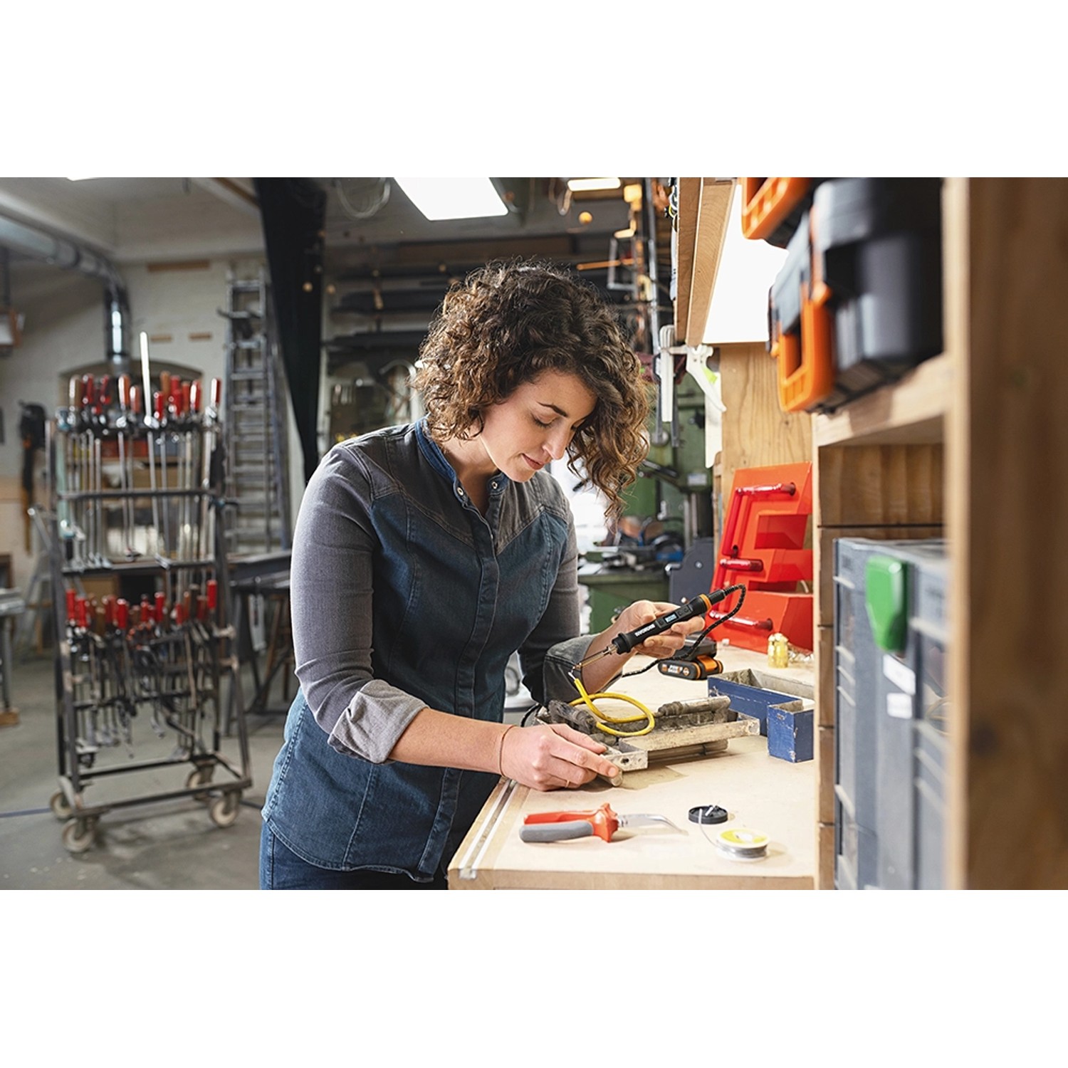 Frau lötet mit Worx MakerX Akku-Lötkolben WX744.9 an Werkbank. Lötgerät mit Zubehör.