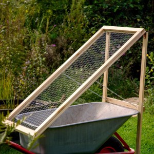 Stehendes Kompostsieb aus Douglasieholz über einer Schubkarre im Garten.