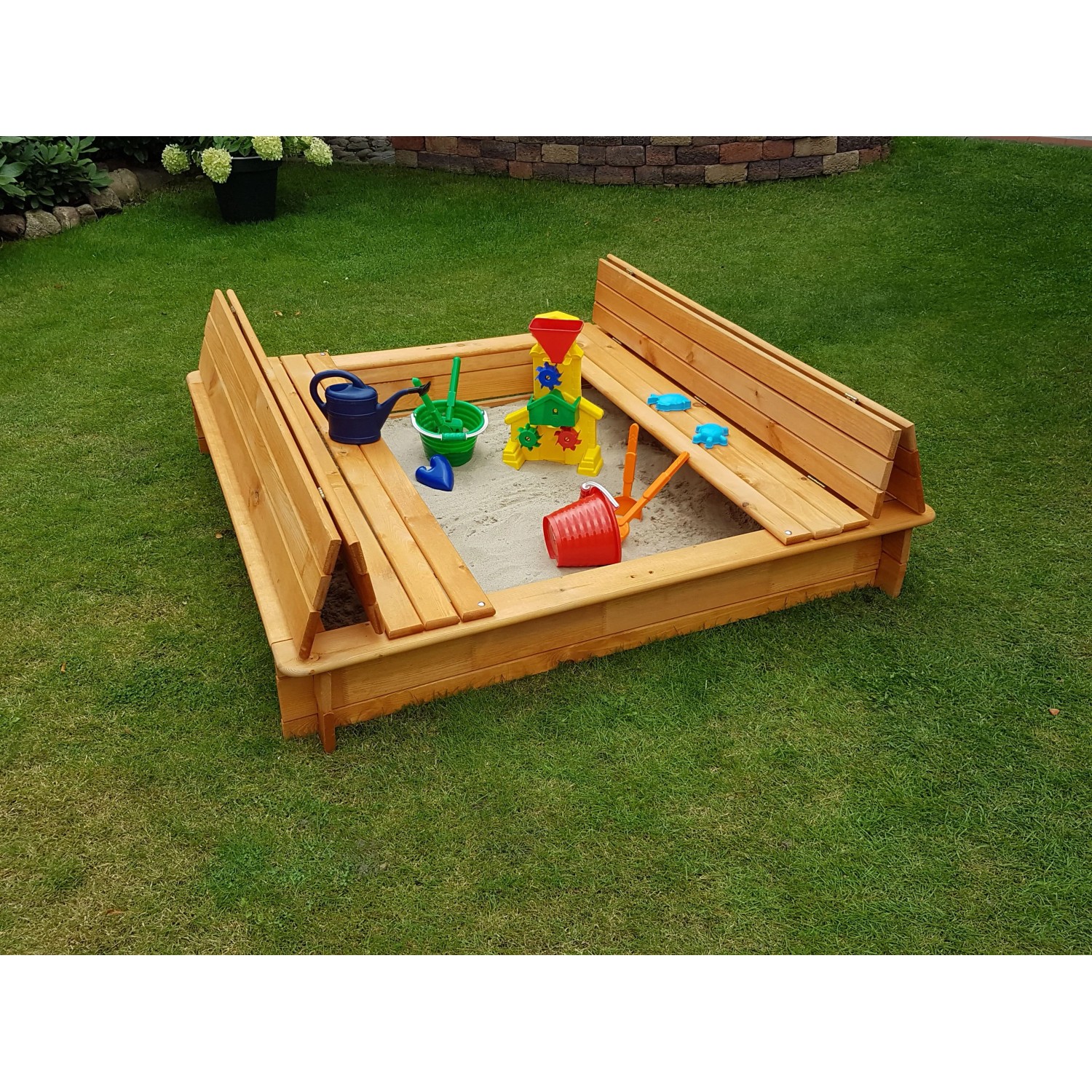 Holz Sandkasten Donald 140x140 cm mit klappbarer Abdeckung und Spielzeug im Garten.