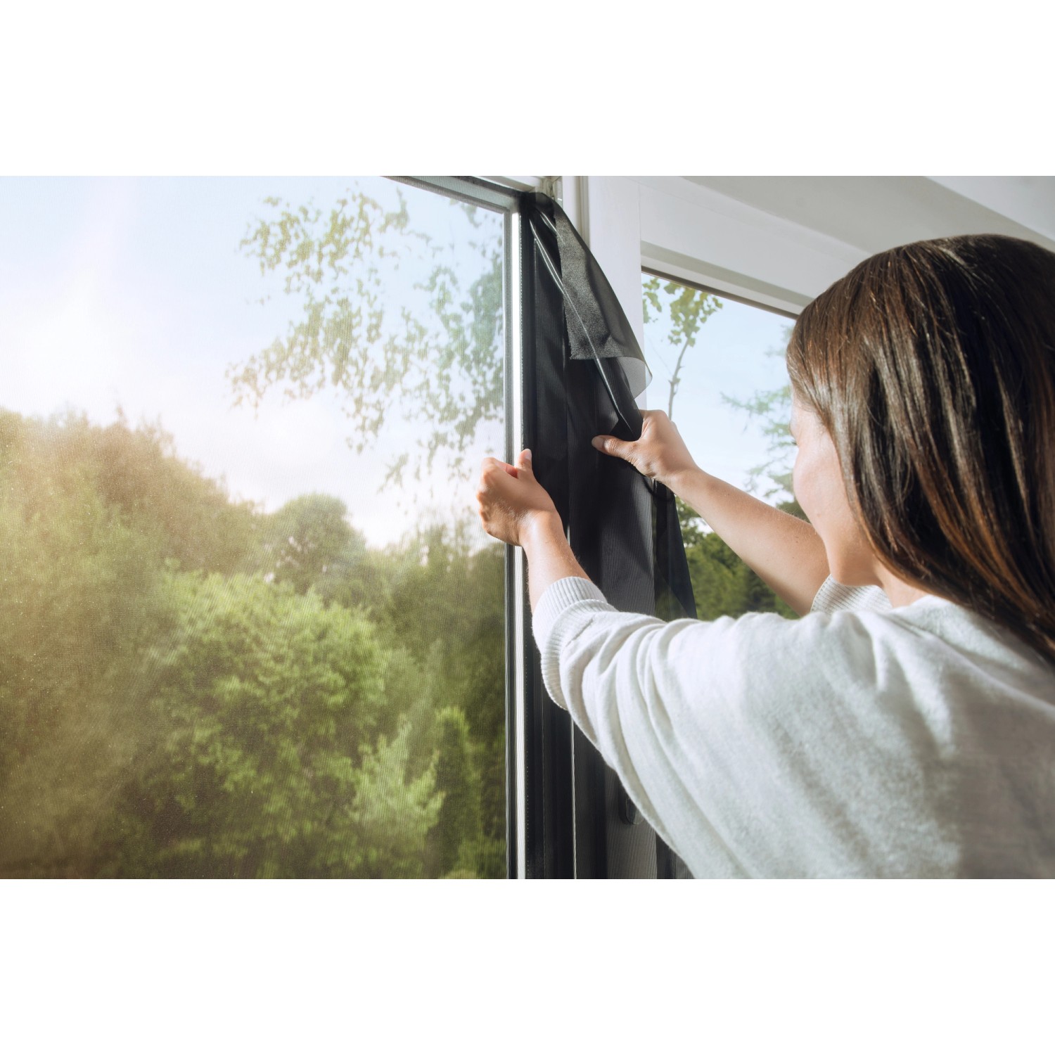 Frau montiert anthrazitfarbenes Tesa Pollenschutzgitter am Fenster.