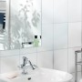 LUX Montageband im Badezimmer: Spiegel, Waschbecken und Armatur an weiß gefliester Wand.