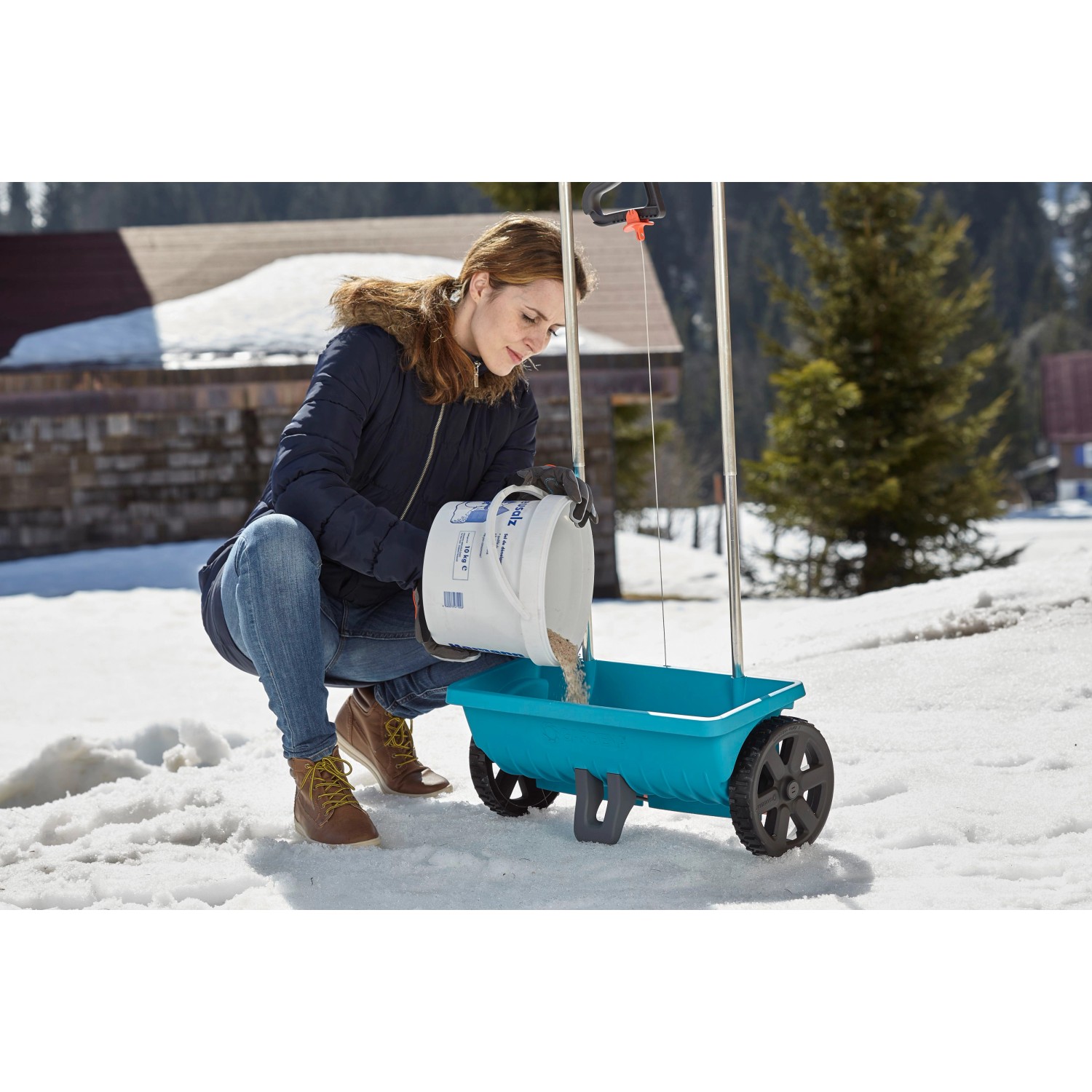Frau befüllt Gardena Streuwagen L im Winter mit Dünger oder Streusalz.