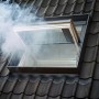 Geöffnetes, weißes Velux Rauchabzugsfenster GGU SK06 auf einem dunklen Ziegeldach mit Rauch.