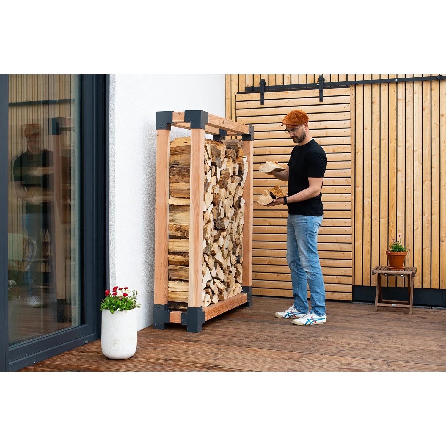 Westmann Kaminholzregal Michel XL aus Lärchenholz (FSC®) mit Holzscheiten und einer Person.