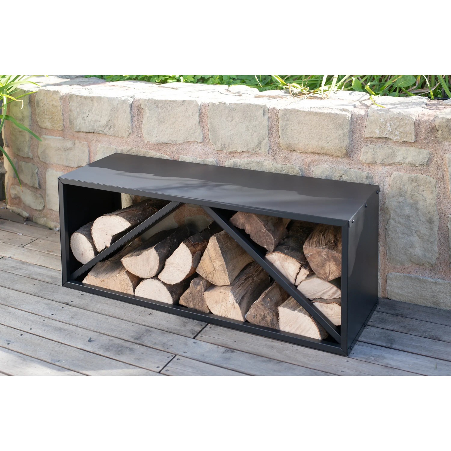 Schwarzes Westmann Kaminholzregal (104x34,5x40cm) mit Holzscheiten vor Steinmauer.
