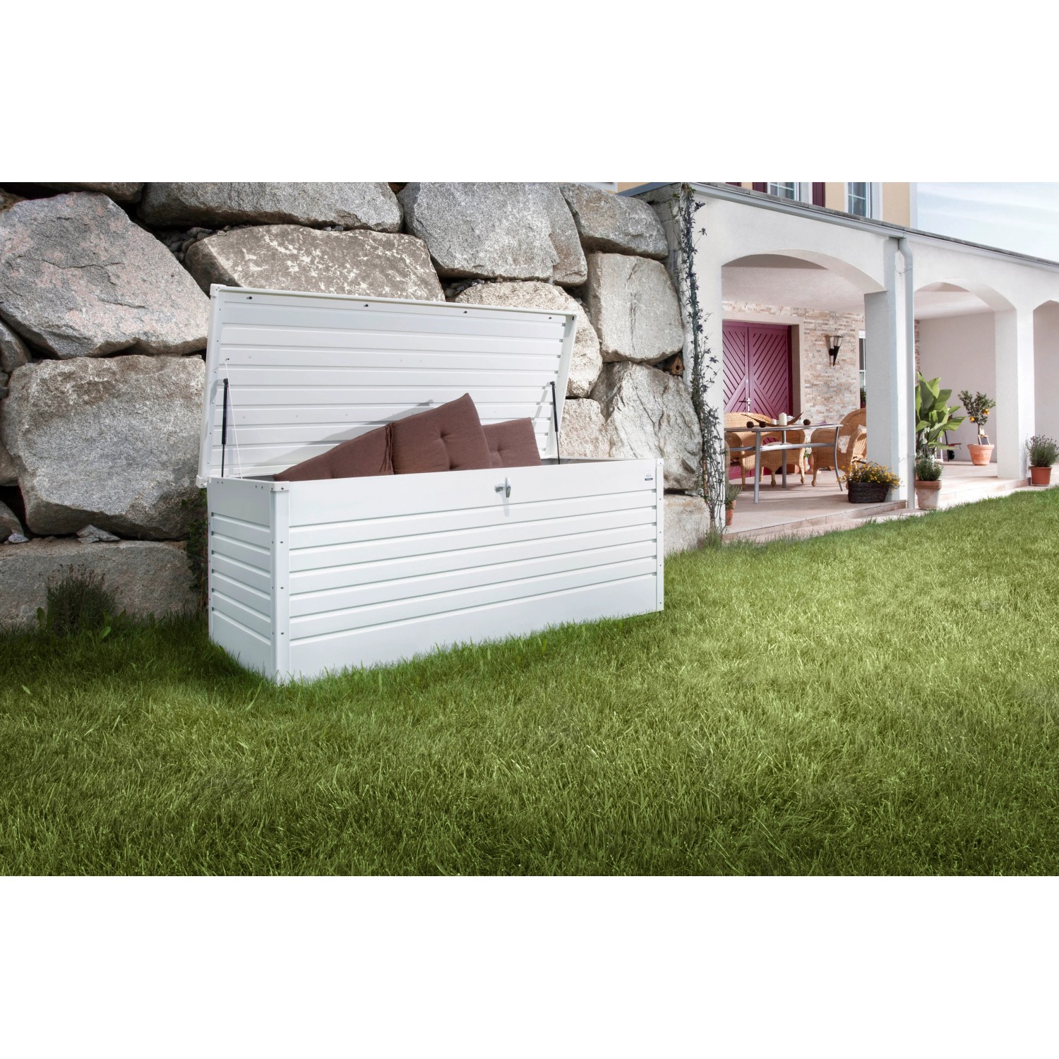 Weiße Biohort Freizeitbox 180 im Garten, geöffnet mit Kissen. Universalbox aus Metall mit Zylinderschloss.