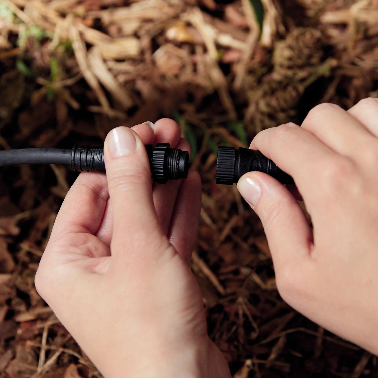 Hände verbinden schwarzes Verlängerungskabel für Philips Hue Gartenstrahler. Einfache Niedervolt-Installation im Garten.