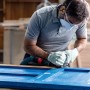 Mann schleift blaue Tür mit Bosch Expert Schleifplatte Multi Material AVZ90 RT4. Zubehör für Multifunktionswerkzeuge.