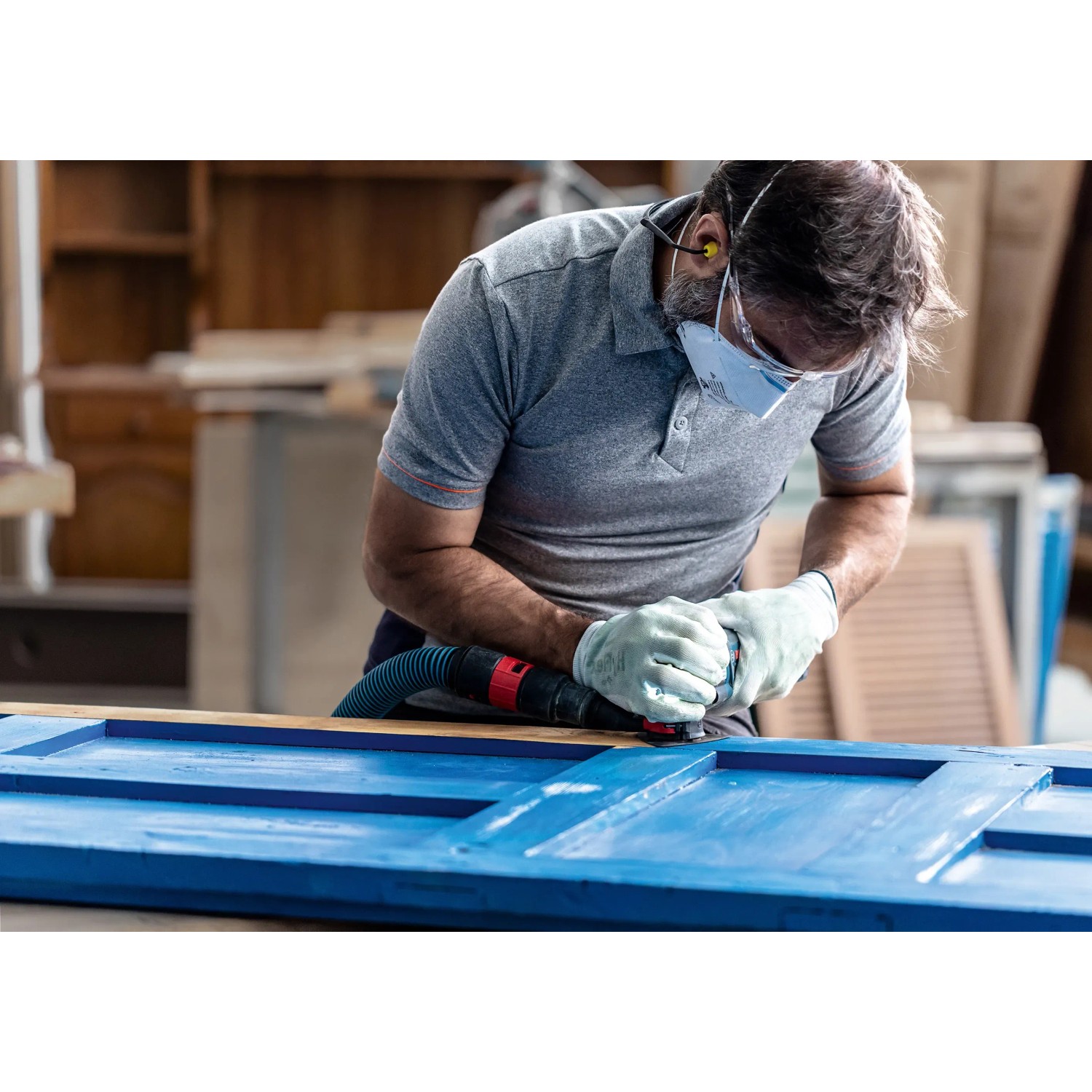 Mann schleift blaue Tür mit Bosch Expert Schleifplatte Multi Material AVZ90 RT4. Zubehör für Multifunktionswerkzeuge.
