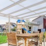 Weiße Gutta Terrassenüberdachung Premium mit Stegplatten und Sitzgruppe im Garten.