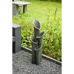 Acqua Arte Wasserspiel Montreux, ein grauer Gartenbrunnen mit vier Trompeten auf Kies.