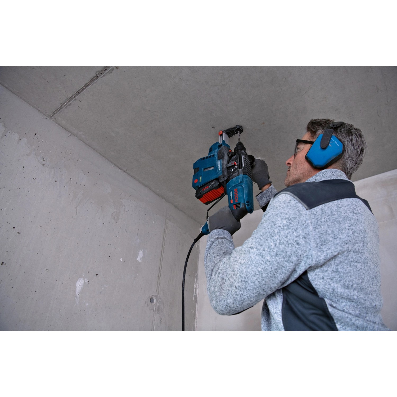 Mann bohrt mit Bosch Professional Bohrhammer GBH 2-26 in Decke. Inkl. Zubehör und L-Case.